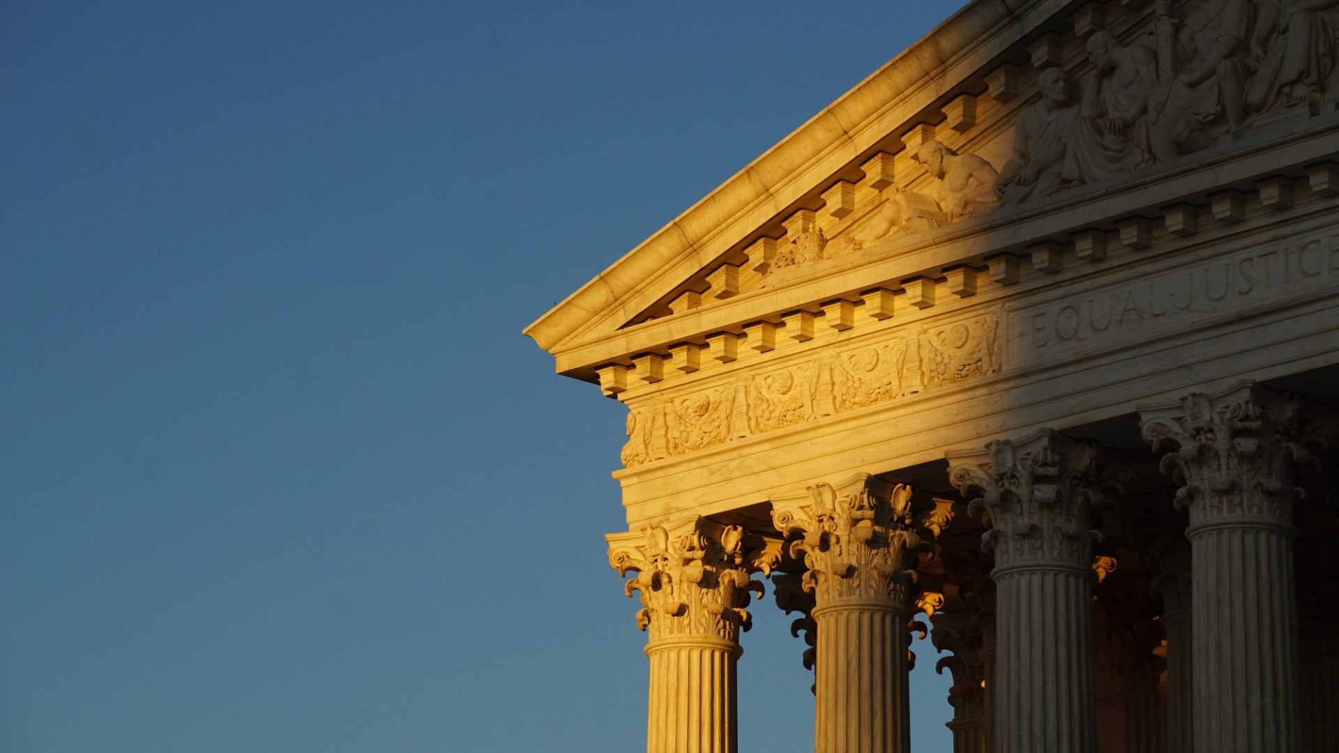 Blue sky in the background with the corner of the Supreme Court building facade in front of it, half of it in the shadow and half of it in the sun