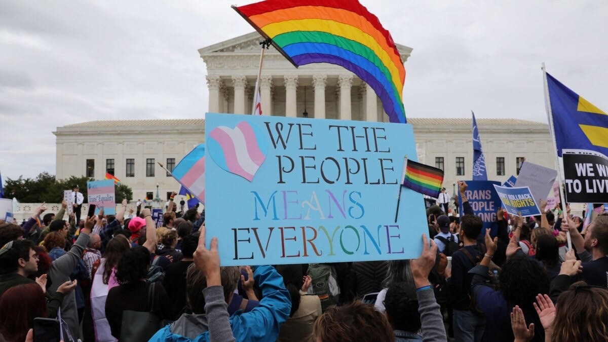 Protesters gather outside courthouse in support of LGBTQ+ rights: main sign reads "We the people means everyone" and is emblazoned with the trans flag